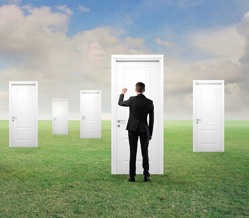 Young businessman knocking at one of many white doors on a green